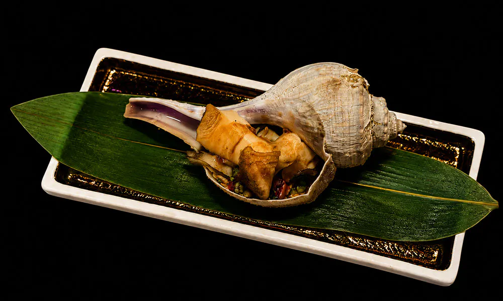 Seasoned conch shell seafood appetizer served on fresh bamboo leaf gold trimmed ceramic plate at Sat Asian Seafood Restaurant &Bar, a Yakitori Restaurant in Flushing