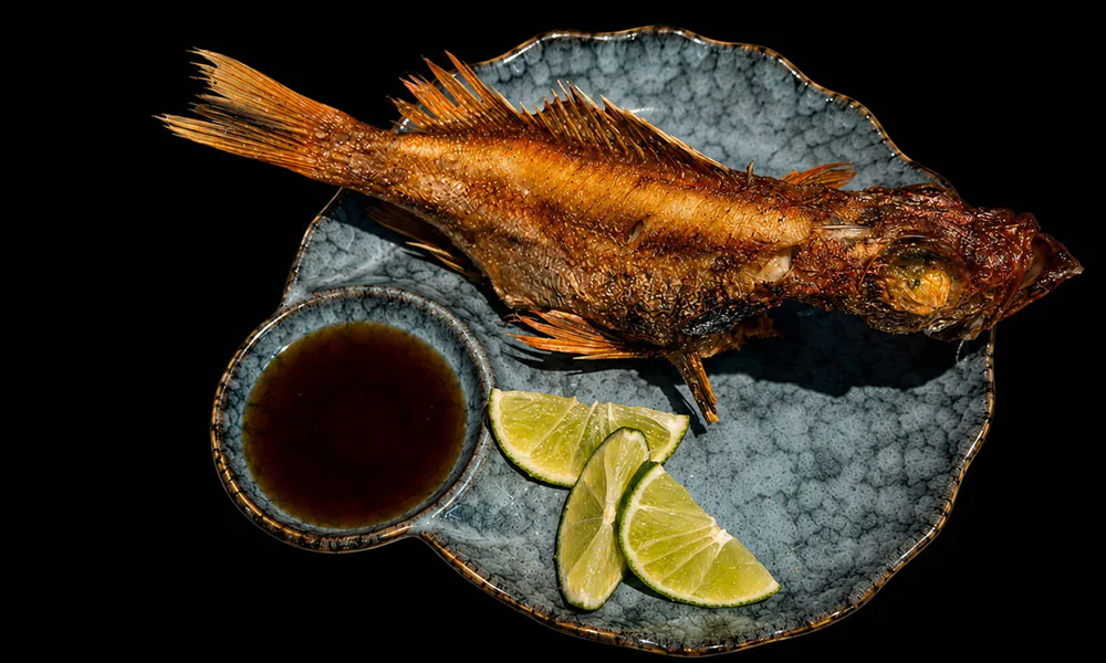 Whole crispy fried fish served with lime wedges and dark soy dipping sauce on textured blue plate at Sat Asian Seafood Restaurant &Bar, a Yakitori Restaurant in Flushing