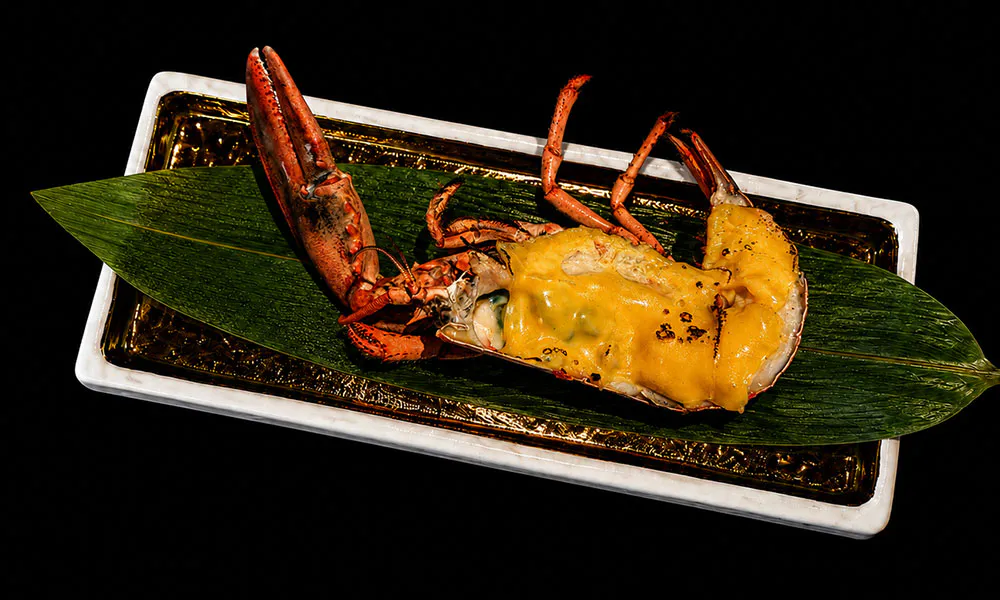 Half baked lobster covered in creamy melted cheese on bamboo leaf gold border plate at Sat Asian Seafood Restaurant &Bar, a Yakitori Restaurant in Flushing