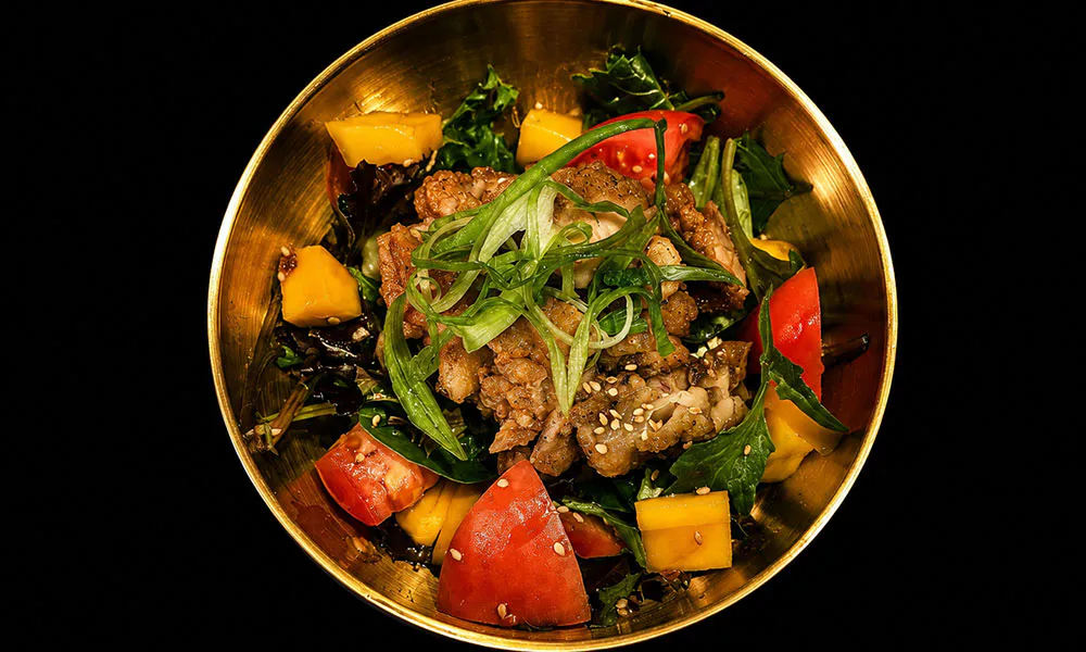 Golden metal bowl salad with fried meat, mango, tomato, greens and sesame seed garnish at Sat Asian Seafood Restaurant &Bar, a Yakitori Restaurant in Flushing