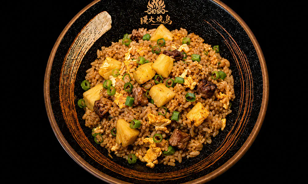 Pineapple beef fried rice with egg, green onion chunks on branded black ceramic bowl at Sat Asian Seafood Restaurant &Bar, a Yakitori Restaurant in Flushing