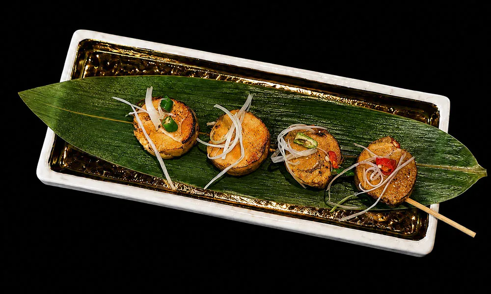 Four grilled scallop skewers topped with shredded onion and chili on bamboo leaf platter at Sat Asian Seafood Restaurant &Bar, a Yakitori Restaurant in Flushing
